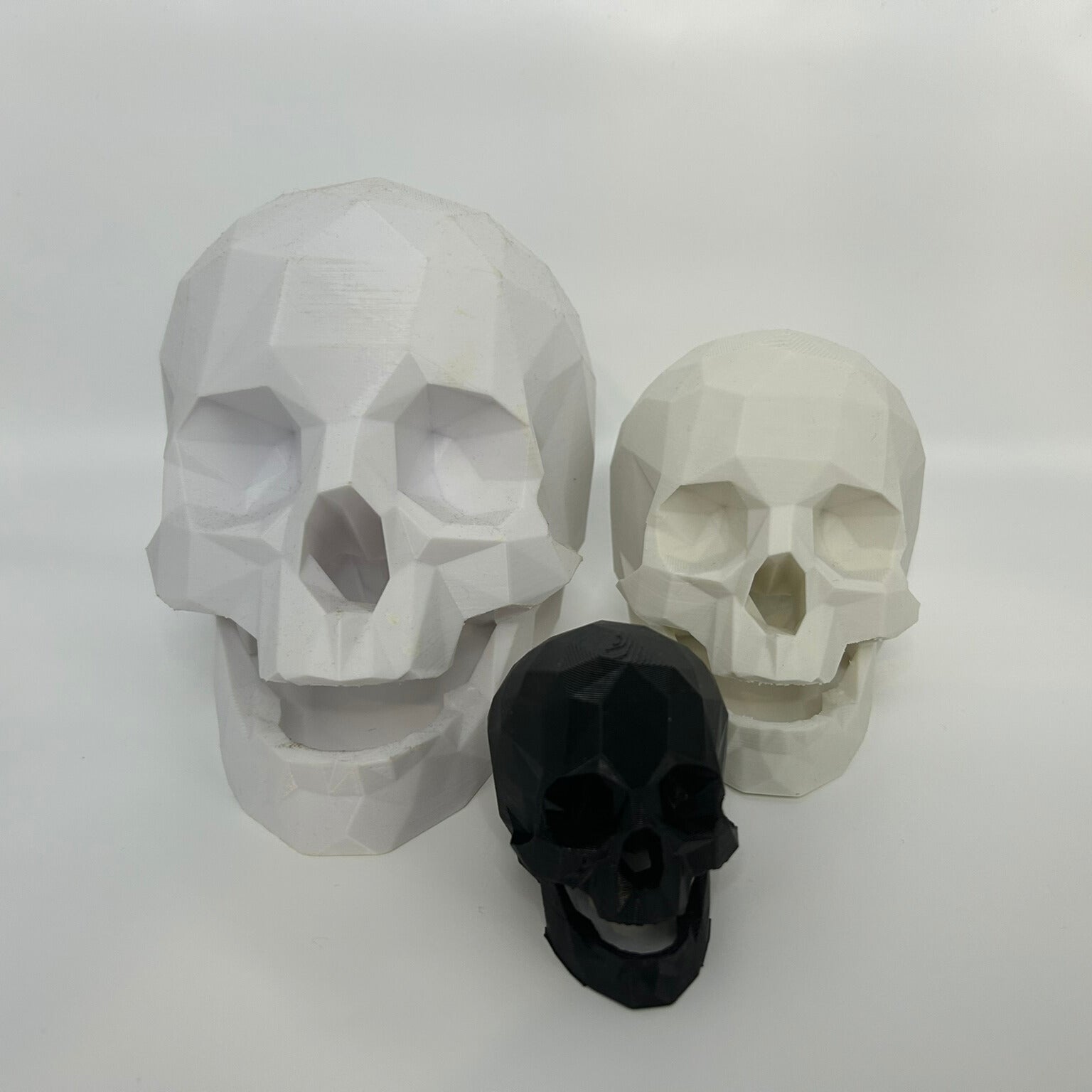 Three low poly decorative skulls, ranging in size Large Medium and Small. Show casing the available colours, black or white.